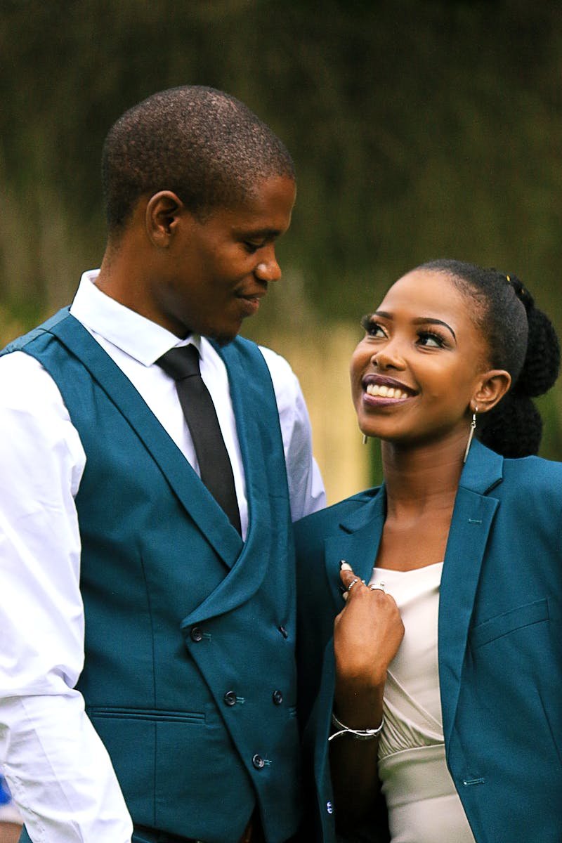 Home Charming couple in matching teal suits, sharing a joyful moment outdoors.
